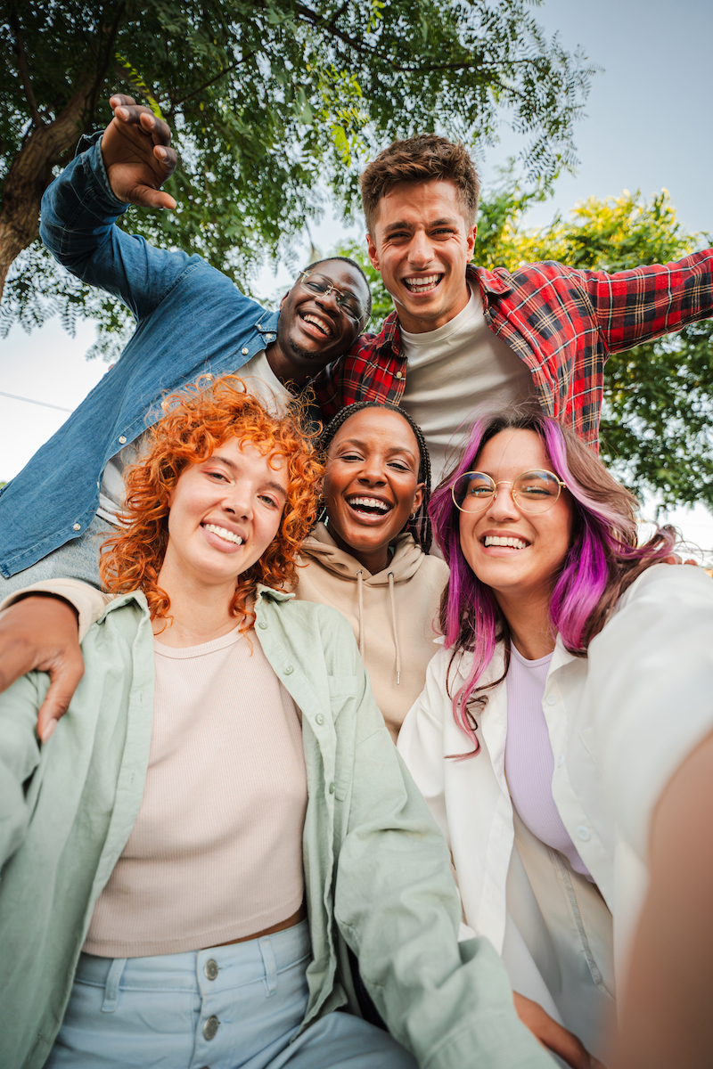 Group of happy teenagers smiling and having fun outdoors, enjoying friendship and diversity while taking a selfie together in a park on a bright sunny day. Young friends smiling and laughing. High quality photo