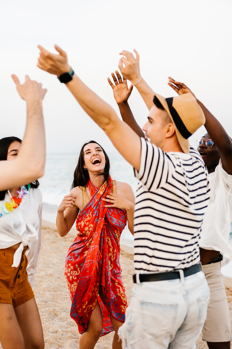 Happy young friends dancing on summer party at beach - Vertical shot of multiracial people having fun together on vacation