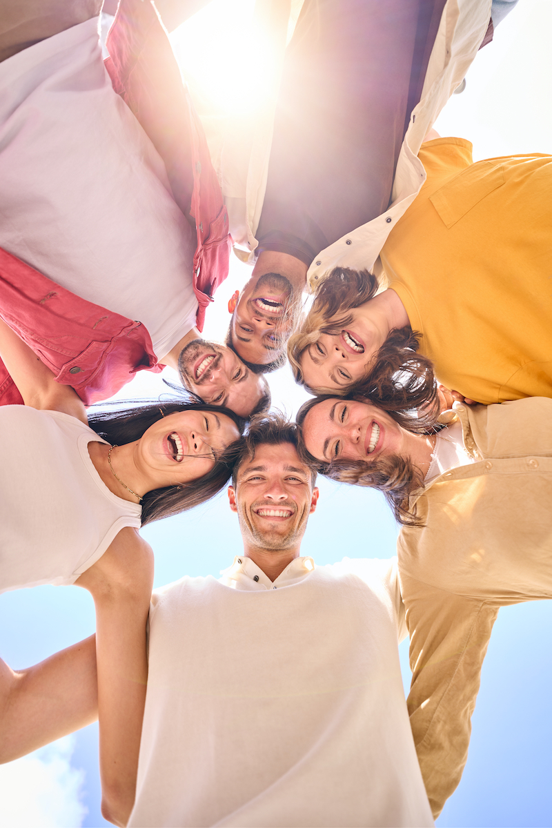 Vertical group of young cheerful multiracial friends looking at camera hugging happy in community.
